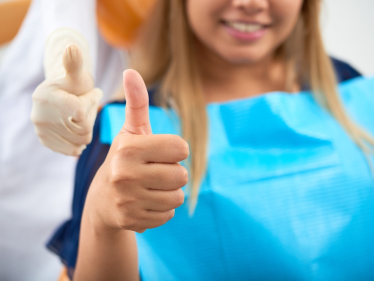 A happy dental patient gives verbal feedback and a thumbs up.