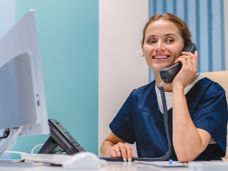 A dental receptionist receives patient feedback on the phone.