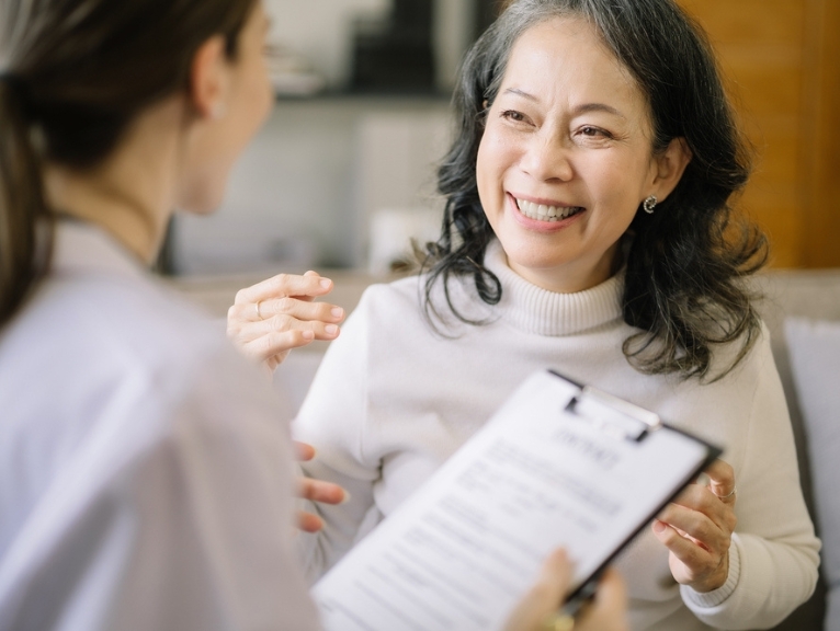 An older lady gives patient feedback on a clipboard to a dentist.