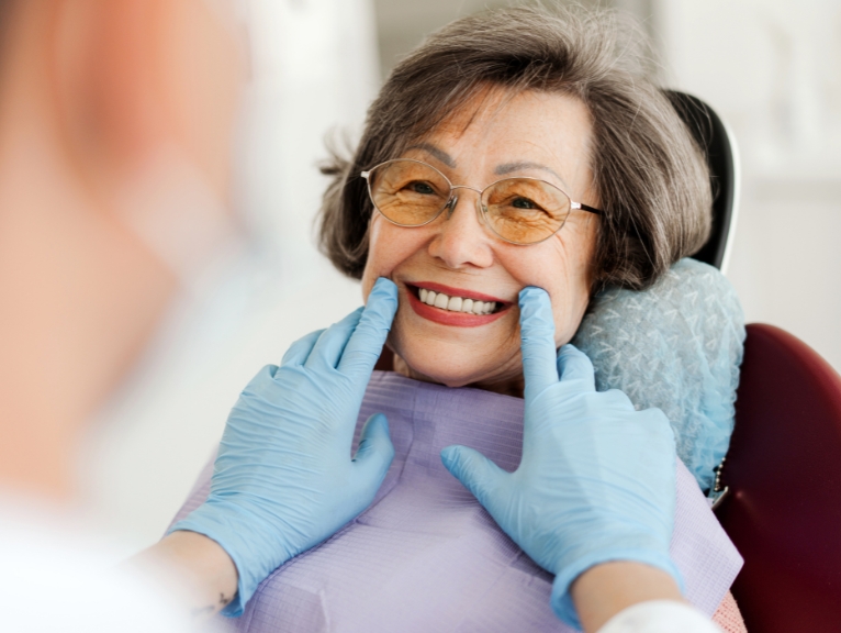 An older patient smiles while a dentist inspects her teeth